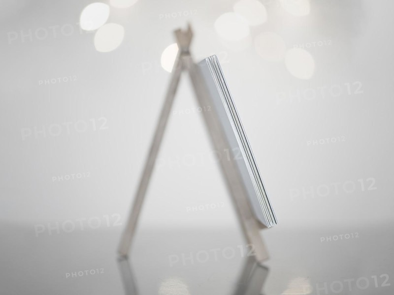Mini easel in white made of wood, standing on a reflective smooth surface, white background with small lights, Germany, Europe