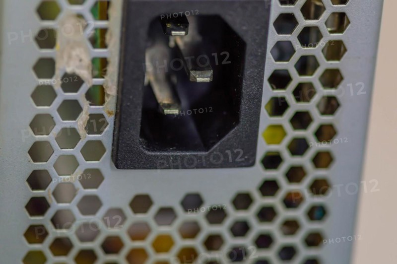 Side view of used computer power supply with focus on male pins of plug that attaches to power cord