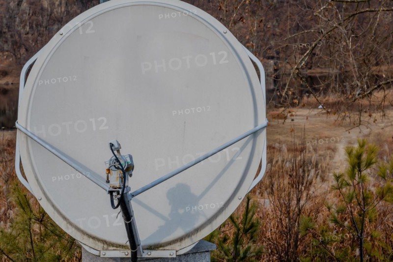Closeup of satellite dish mounted on concrete column with riverside slightly blurred in background in South Korea