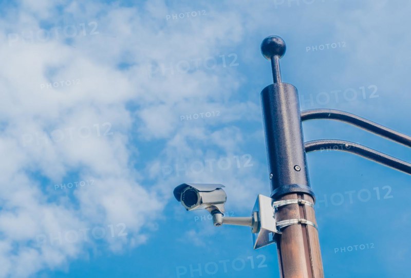 Surveillance camera mounted on metal light pole with blue sky and puffy white clouds in background in South Korea