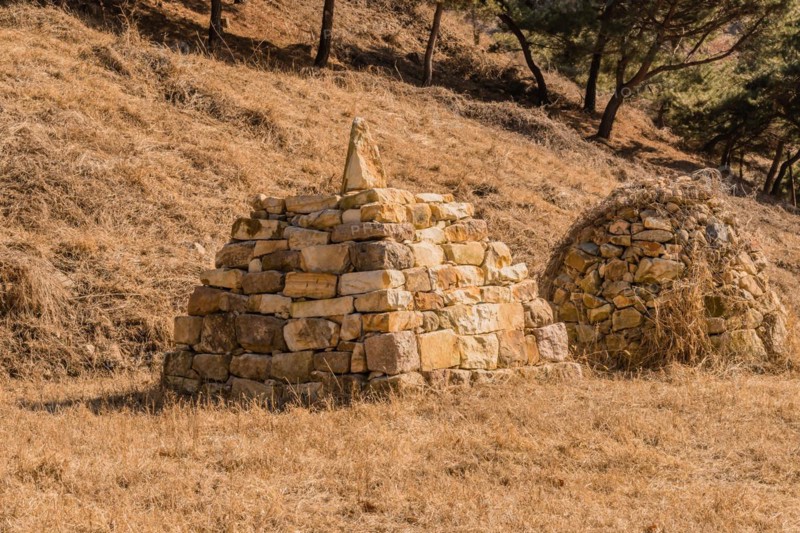 Two pyramid shaped rock structures in field of brown grass at foot of hillside in Boeun, South Korea, Asia