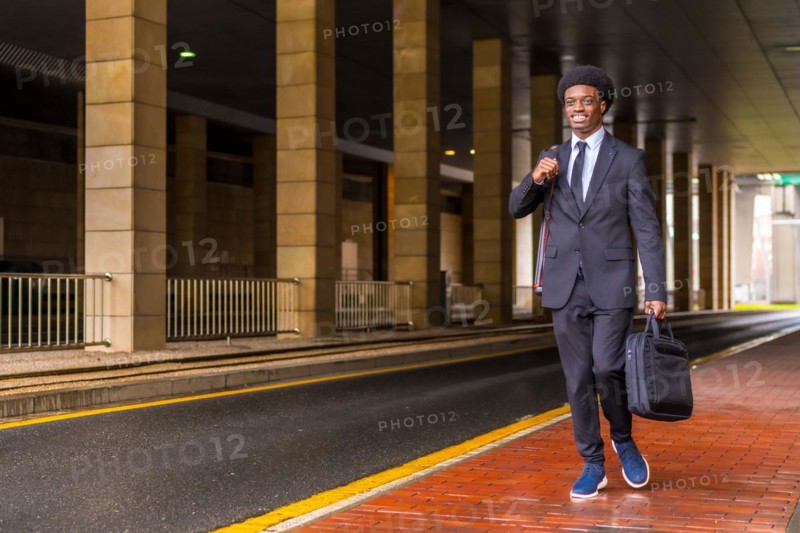 Horizontal photo with copy space of an african architect holding computer bag and drawings tube walking in the city