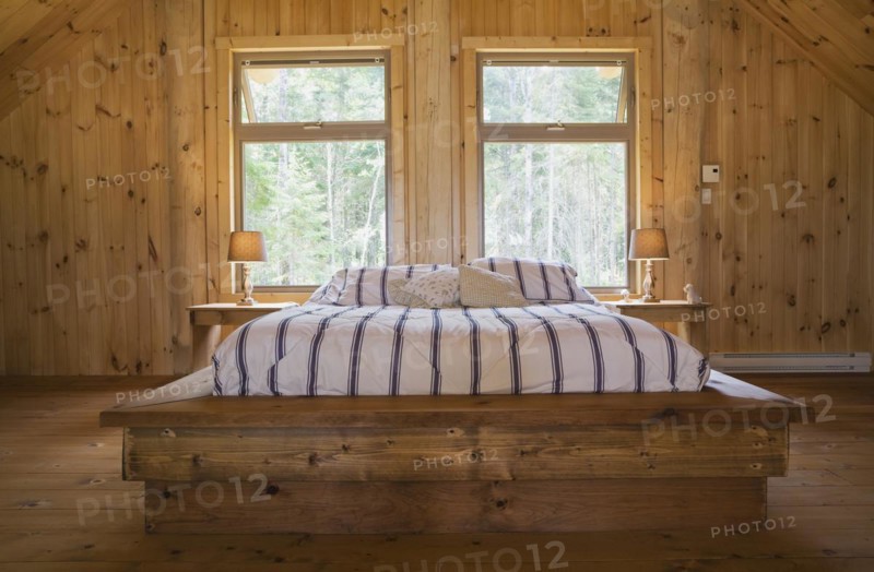 King size bed with wooden frame in master bedroom on upstairs floor inside handcrafted Eastern white pine Scandinavian log cabin home, Quebec, Canada, North America