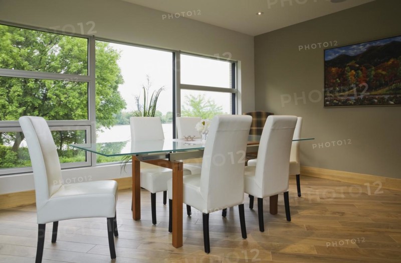 Clear glass top table with white leather high back chairs in dining room with beige ceramic tile floor inside modern cubist style home, Quebec, Canada, North America