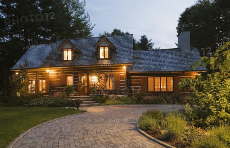 Illuminated old 1800s reconstructed log cabin home facade and paving stone driveway at dusk, Quebec, Canada, North America