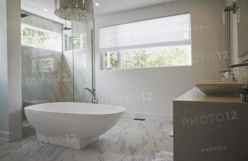Glass shower stall with white acrylic freestanding bathtub in main bathroom with marble floor tiles inside luxurious home, Quebec, Canada, North America