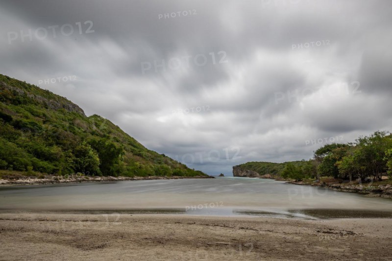 Rocky coast, long bay by the sea at sunset. Dangerous view of the Caribbean Sea. Tropical climate on a cloudy day in La Porte d'Enfer, Grande Terre, Guadeloupe, French Antilles, North America