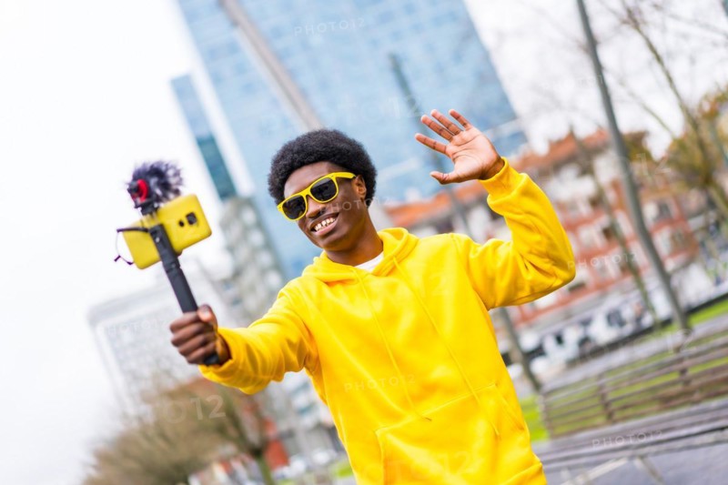 Cool african young content creator waving at camera steaming live standing in a city