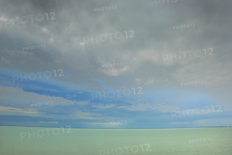 A serene seascape with a calm sea under a blue sky with wispy clouds