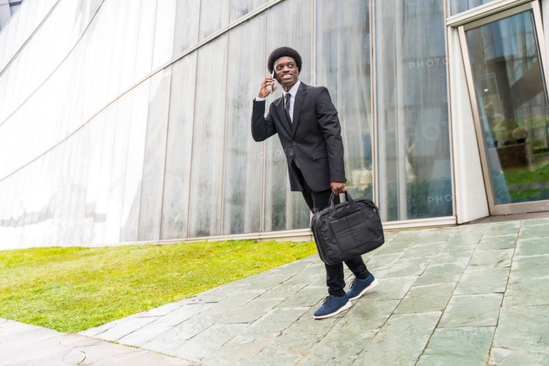 Full length portrait of a cool african businessman talking to the mobile walking in the city