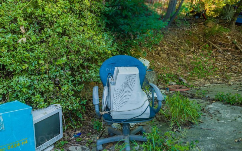 Old CRT computer monitors discarded in rural wooded area. One in old chair the other on the ground next to blue container in Seoul, South Korea, Asia