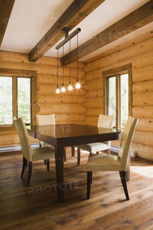 Brown wooden table and white cotton cloth upholstered high back chairs in dining room inside contemporary style log home, Quebec, Canada, North America