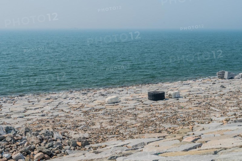 Wide view of a rocky coast polluted with waste and a tire, in South Korea