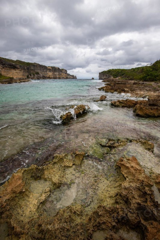Rocky coast, long bay by the sea at sunset. Dangerous view of the Caribbean Sea. Tropical climate on a cloudy day in La Porte d'Enfer, Grande Terre, Guadeloupe, French Antilles, North America