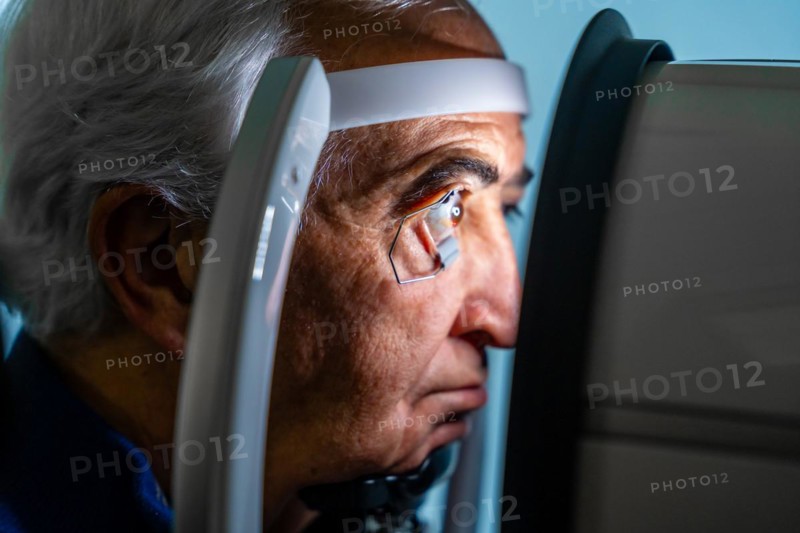 Close-up photo of a serious senior man with eye opener looking through an innovative machine during a laser treatment for glaucoma