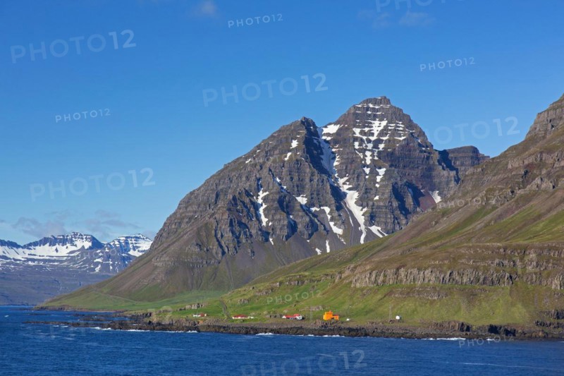 Rugged mountains and orange lighthouse at Skalanes along the fjord Seyoisfjoerour, Seydisfjoerdur in summer, Eastern Region, Austurland, Iceland, Europe