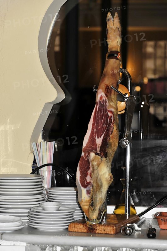 Jaen, A Jamon Iberico on a wooden board next to a pile of plates in a restaurant, Jaen, Andalusia, Spain, Europe