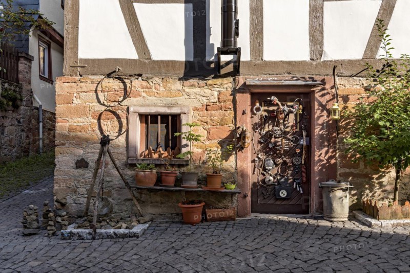 Old half-timbered house, whimsically decorated, stone towers, tripod with pendulum, flower pots, door with masks, skulls, engine parts, cartridge cases, tools, old town, Ortenberg, Vogelsberg, Wetterau, Hesse, Germany, Europe
