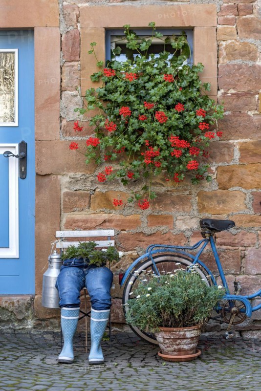 Curious decoration on a front door, blue jeans trousers in rubber boots with flower pot, geraniums, old bicycle, idyll, old town, Ortenberg, Wetterau, Vogelsberg, Hesse, Germany, Europe