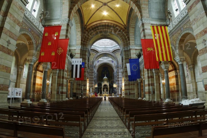 Marseille Cathedral or Cathedrale Sainte-Marie-Majeure de Marseille, 1852-1896, Marseille, View through the nave of a church with pews and various flags on the pillars, Interior view of a church with arches, flags and a row of pews, Marseille, Departement Bouches du Rhone, Region Provence Alpes Cote d'Azur, France, Europe