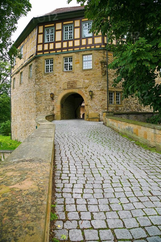 Access to the moated castle Sachsenheim, Grosssachsenheim Castle, former moated castle, archway, cobblestones, path, wall, bridge, crossing, stone figure on the left, relief of the legendary figure Klopferle, castle ghost, coat of arms, with inscription, exterior lights, lamps, architecture, historical building from the 15th century, Sachsenheim, Ludwigsburg district, Baden-Wuerttemberg, Germany, Europe