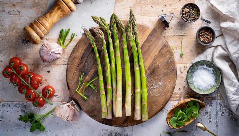 Fresh asparagus on a wooden board surrounded by tomatoes, garlic and spices, ready to cook, green asparagus, asparagus spears, KI generated, AI generated