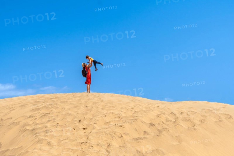 Mother lifting child smiling in the dunes of Maspalomas in summer, Gran Canaria, Canary Islands
