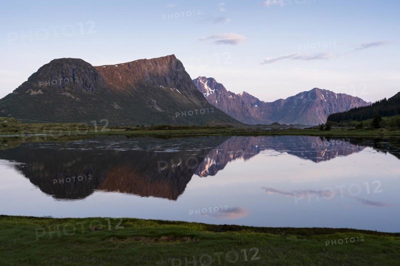 Landscape on the Lofoten Islands. Vagspollen bay, with Offersoykammen mountain behind it. The mountain Stornappstinden on Flakstadoya in the background. The mountains are reflected in the water. At night at the time of the midnight sun in good weather. Early summer. Vestvagoya, Lofoten, Norway, Europe