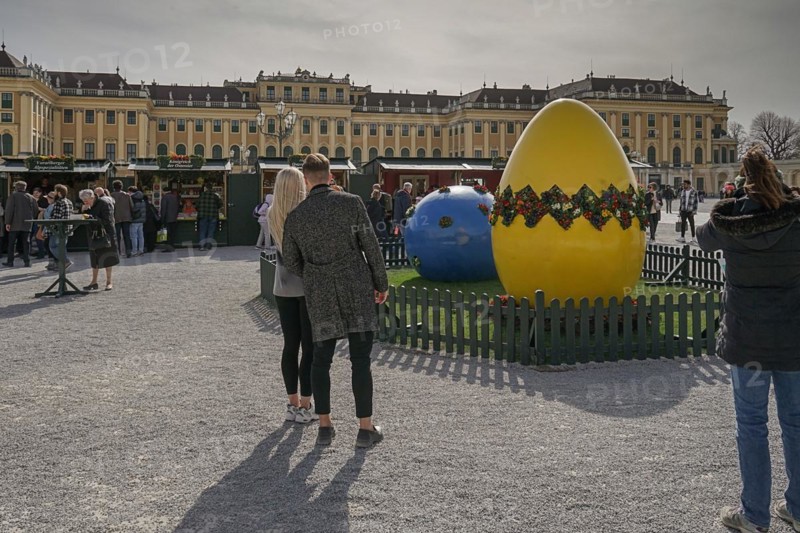 A couple looks at a large, decorative Easter egg in front of the magnificent Schoenbrunn Palace Easter Market