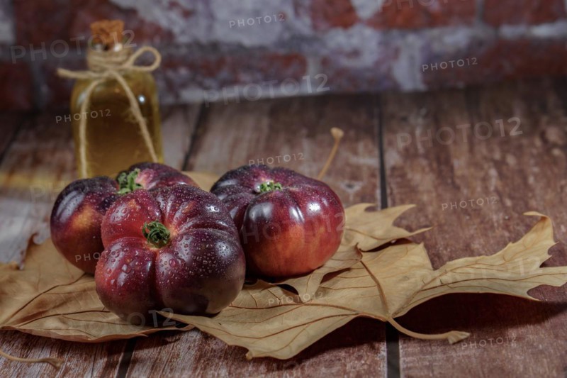 Group of tasty fresh tomatoes of the blue variety with drops of water on dry leaves next to ears of wheat with a bottle of olive oil in the background