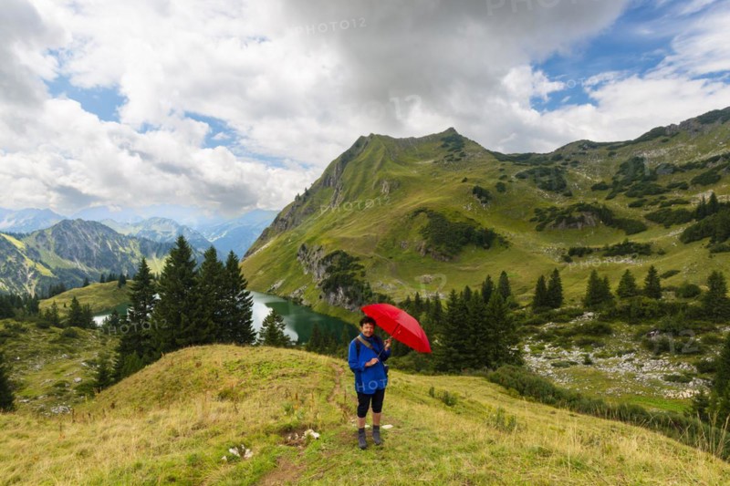 Woman 60-65 hiking with umbrella, behind her Seealpsee and Seekoepfel, 1919m, Allgaeu Alps, Allgaeu, Bavaria, Germany, Europe