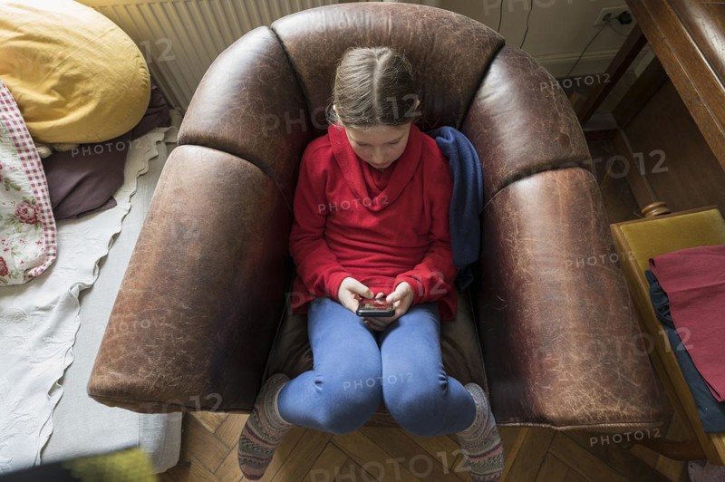 Symbol photo mobile phone, internet, addiction, little girl, 10 years old, sitting in an armchair with her mobile phone, Mecklenurg-Vorpommern, Germany, Europe