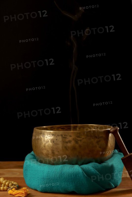 Tibetan singing bowl smoking on green cloth next to a Buddhist japa mala isolated on black background with copy space
