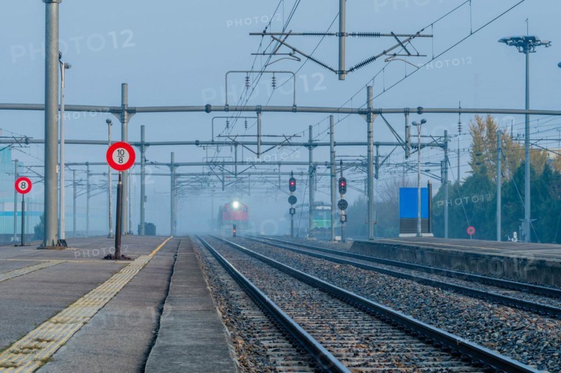 Desolate railway station in foggy conditions at dawn with signal lights on and a train approaching, in South Korea