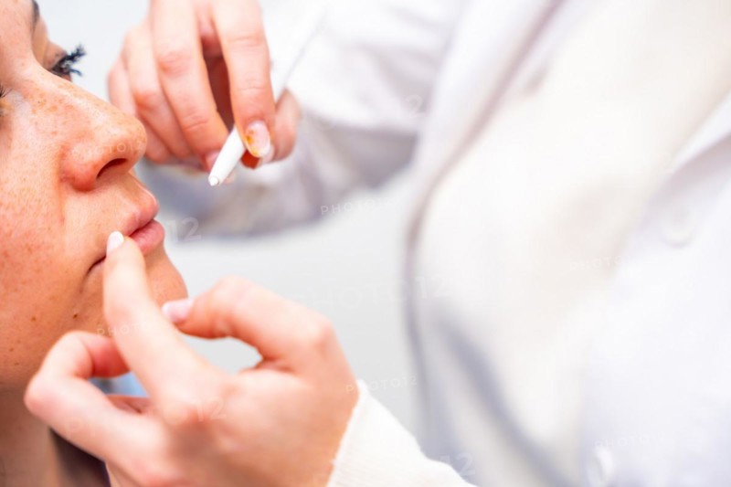 Close-up of the hands of a cosmetologist marking middle-aged woman's face for beauty treatment
