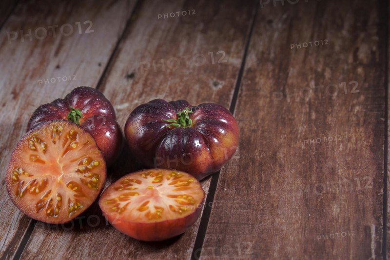 Group of tasty fresh tomatoes of the blue variety with a halved tomato dipped in water drops on a wooden table dipped in water drops on a wooden table