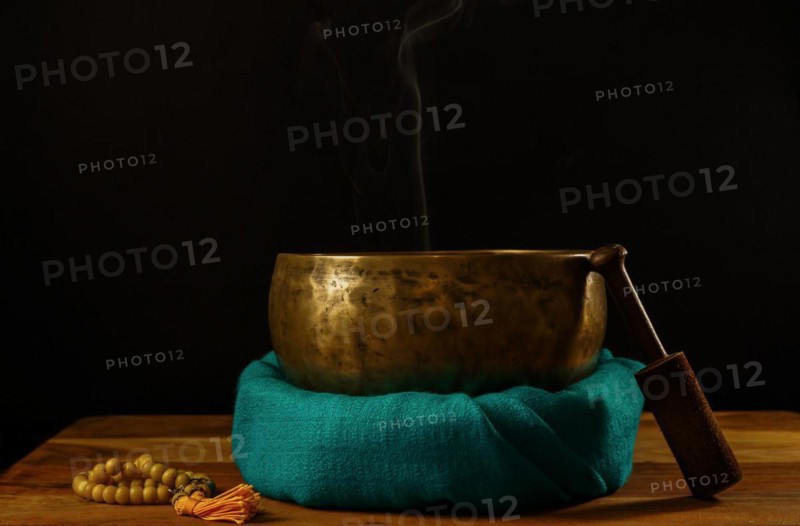 Tibetan singing bowl smoking on green cloth next to a Buddhist japa mala isolated on black background with copy space