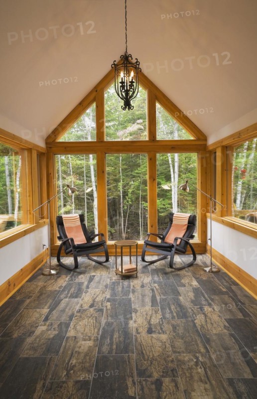 Reading room with tan and dark grey nuanced ceramic tile floor and two black leather rocking chairs plus pendant medieval candle light bulb style black wrought iron chandelier inside luxurious contemporary timber framed and milled log cabin home, Quebec, Canada, North America