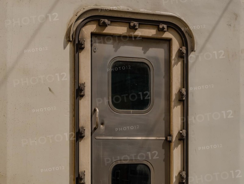 Close-up of a metallic train door with a small window and rivets, in South Korea