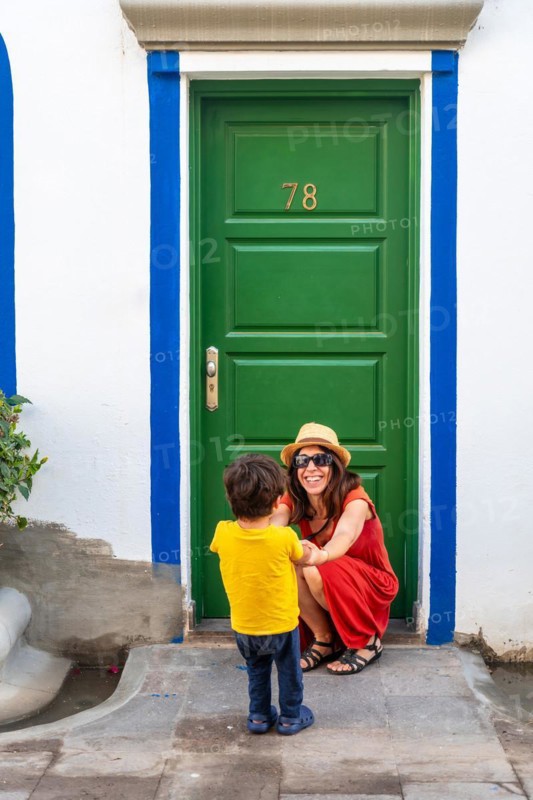 A woman and a child are standing in front of a green door with the number 78 on it
