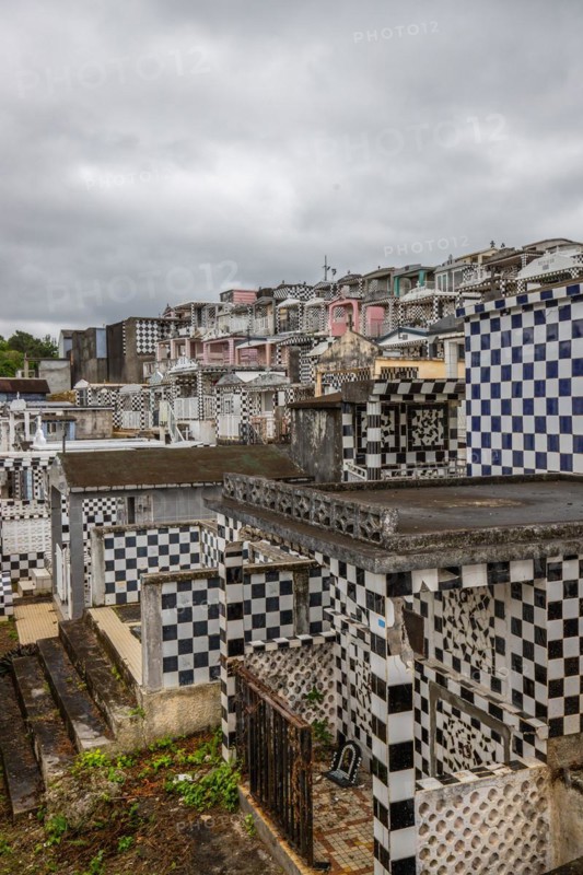 Famous cemetery, many mausoleums or large tombs decorated with tiles, often in black and white. Densely built buildings under a dramatic cloud cover Cimetiere de Morne-a-l'eau, Grand Terre, Guadeloupe, Caribbean, North America