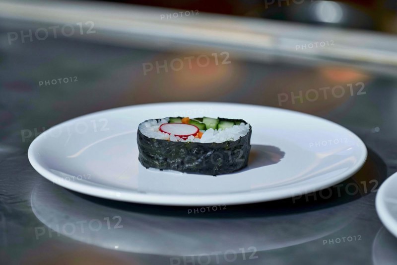 A piece of sushi with rice and cucumber wrapped in seaweed on a plain white plate, AI generated