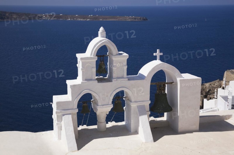 White roughcast cladded arched church bells tower with cross overlooking the Aegean sea, Oia village, Santorini, Greece, Europe