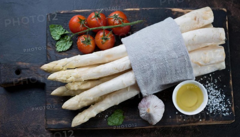Bunch of white asparagus on a wooden board with tomatoes, garlic and oil, bunch of white asparagus wrapped in a damp kitchen towel, KI generated, AI generated