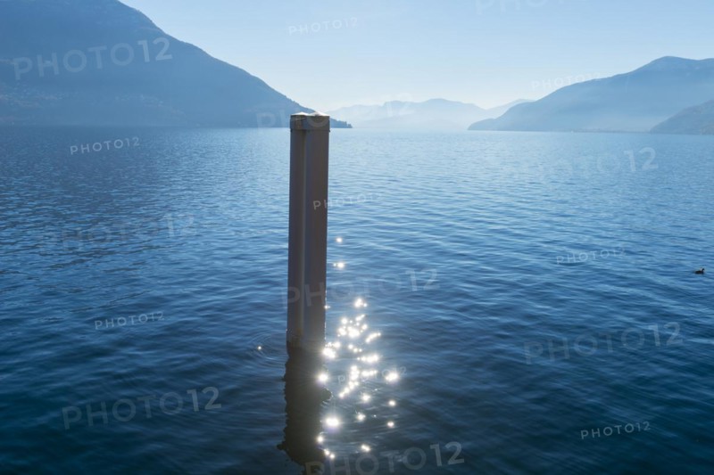 Pole with Sun Reflection on Lake Maggiore with Mountain in Ascona, Ticino, Switzerland, Europe