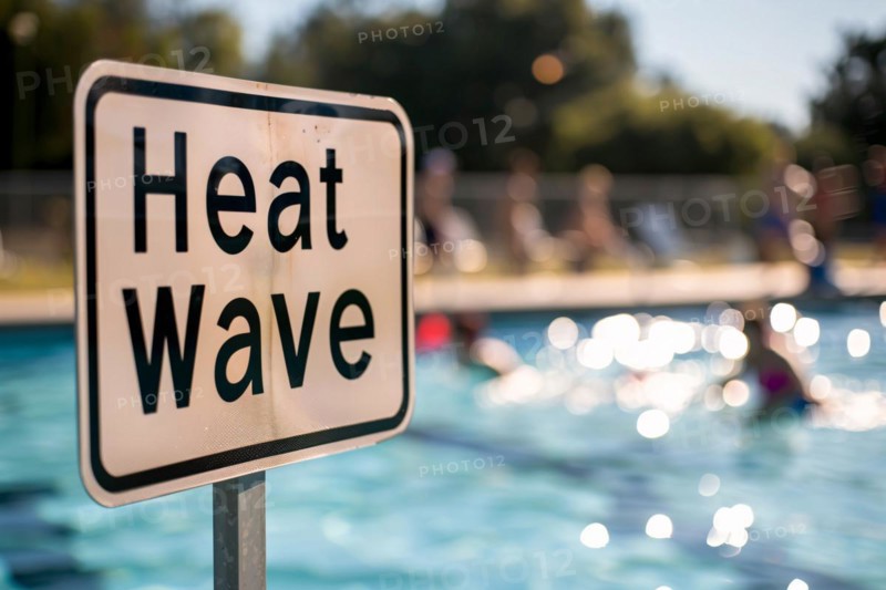 Sign with text 'Heat wave' in front of blurry public swimming pool with people. KI generiert, generiert, AI generated