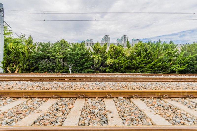 Railway tracks on a bright day with lush green foliage and city buildings under a sky with fluffy clouds, in South Korea