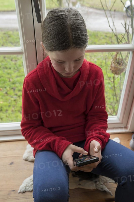Girl, 10 years old, sitting on the windowsill with mobile phone, Mecklenburg-Vorpommern, Germany, Europe