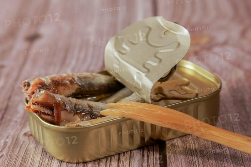 Tin can with tasty sprats with a wooden fork on a wooden table