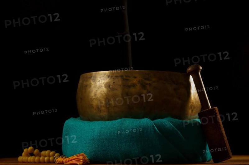 Tibetan singing bowl smoking on green cloth next to a Buddhist japa mala isolated on black background with copy space